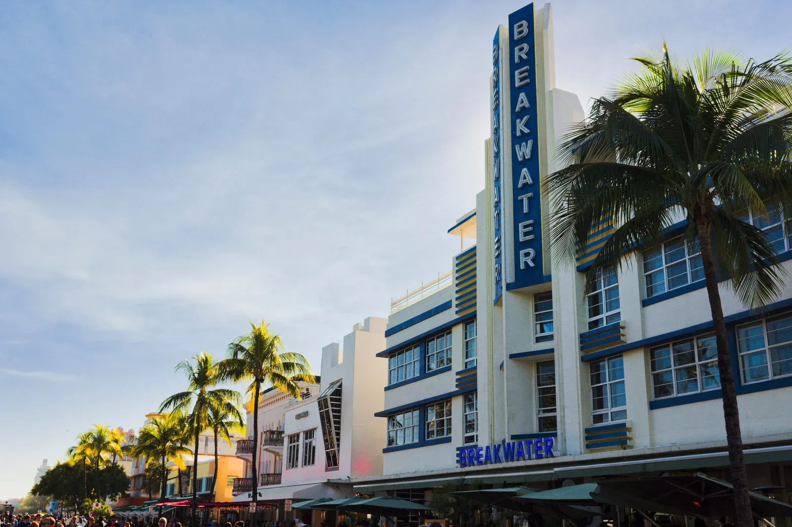 The Breakwater Hotel's tall blue and yellow vertical neon sign and Streamline Moderne facade on Ocean Drive in Miami Beach during the day