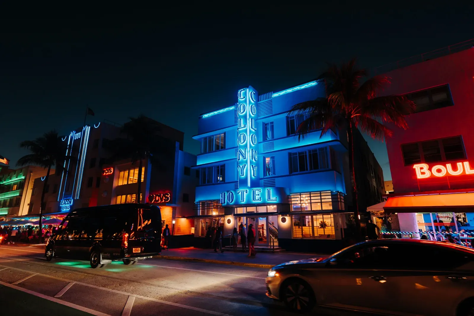 The Colony Hotel's blue vertical neon sign glowing above its Art Deco facade on Ocean Drive in Miami Beach at night
