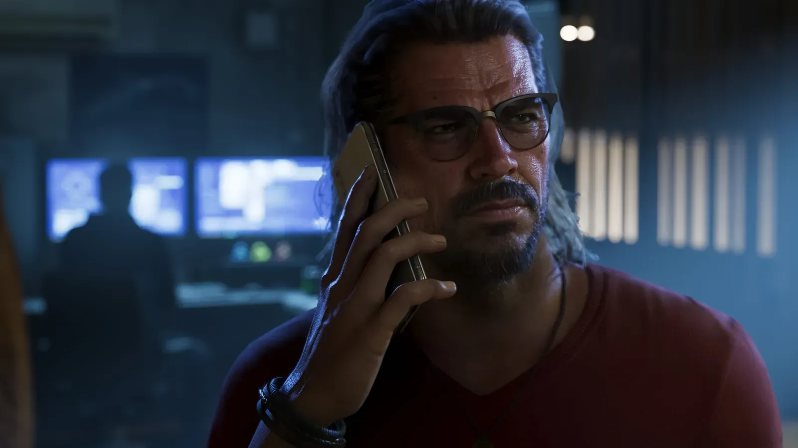 Raul Bautista al teléfono en una habitación poco iluminada llena de monitores en GTA 6